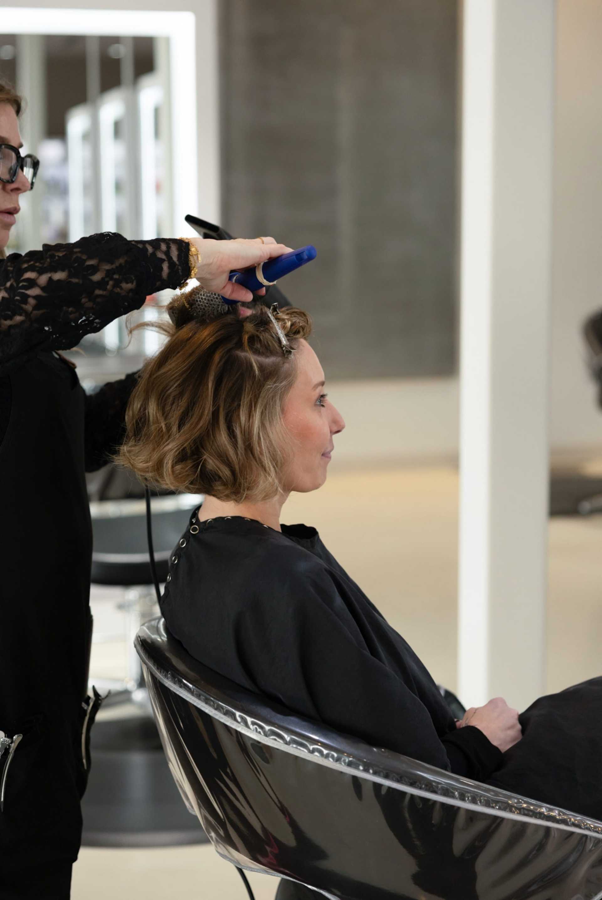 Woman getting hair styled in a salon, hairstylist using a brush and blow dryer.