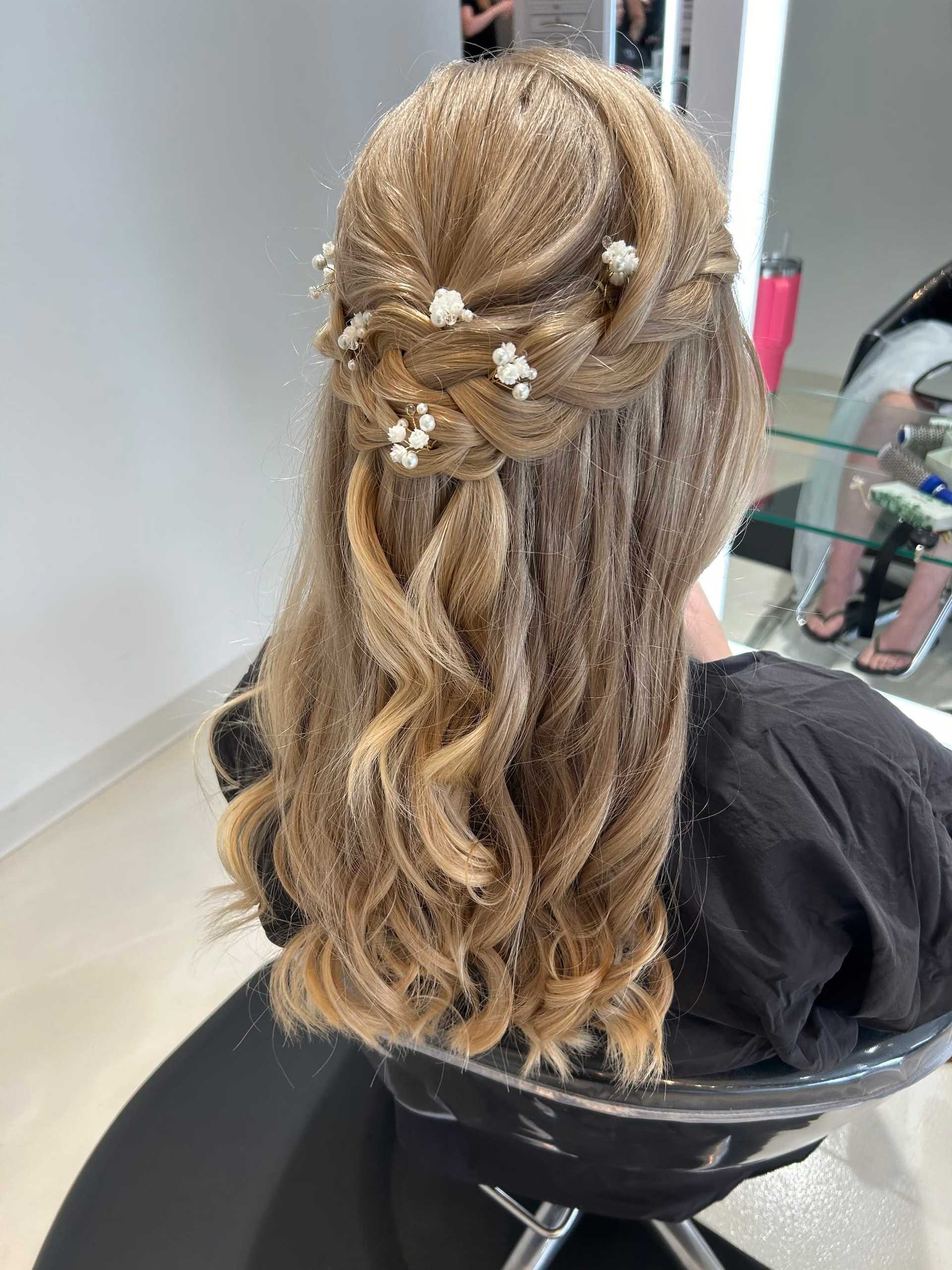 Elegant braided hairstyle with pearl accents on long blonde hair in a salon setting.